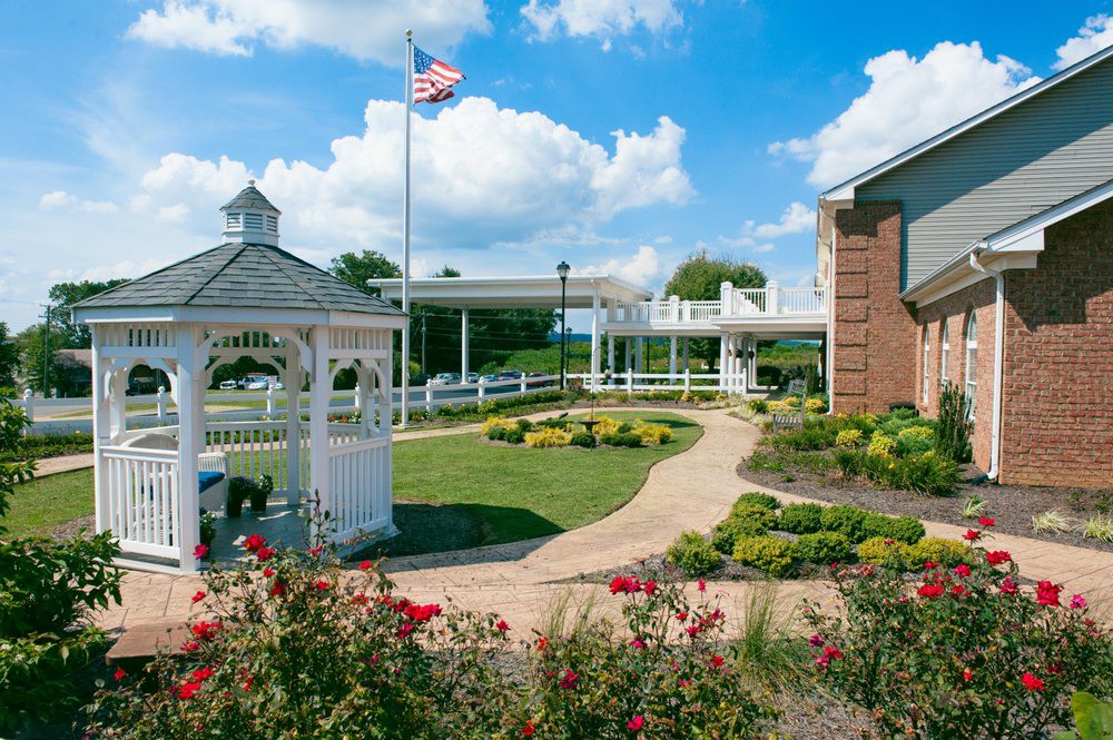 A serene garden with a gazebo, pathway, and American flag waving under a blue sky.