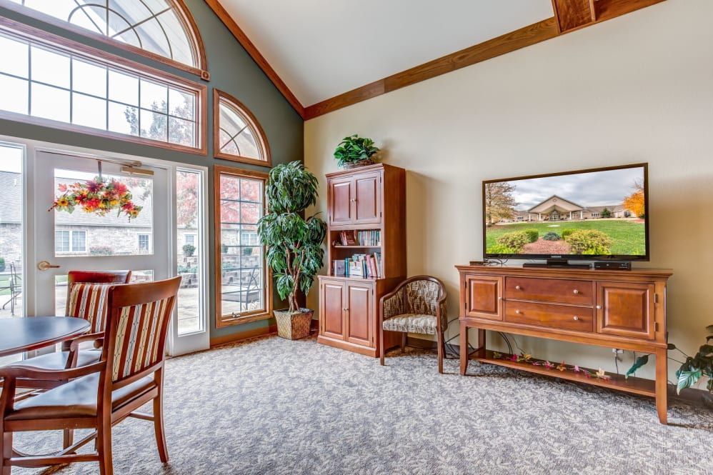 A cozy living room with large arched windows, wooden furniture, and a potted plant.