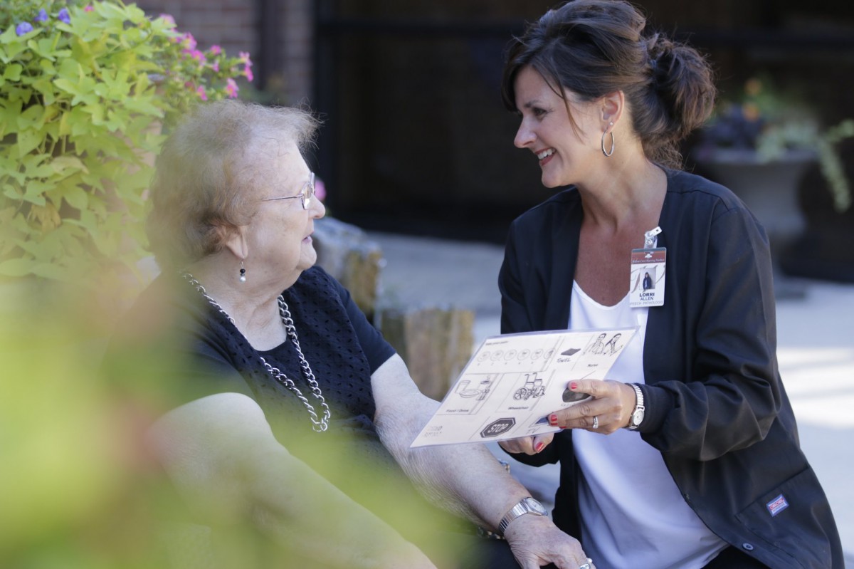 A caregiver converses with an elderly woman outdoors.