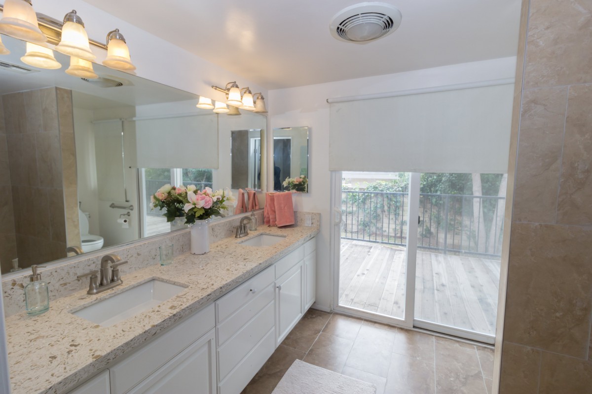 A bright and modern bathroom with a large mirror, twin sinks, decorative flowers, and ample natural light.