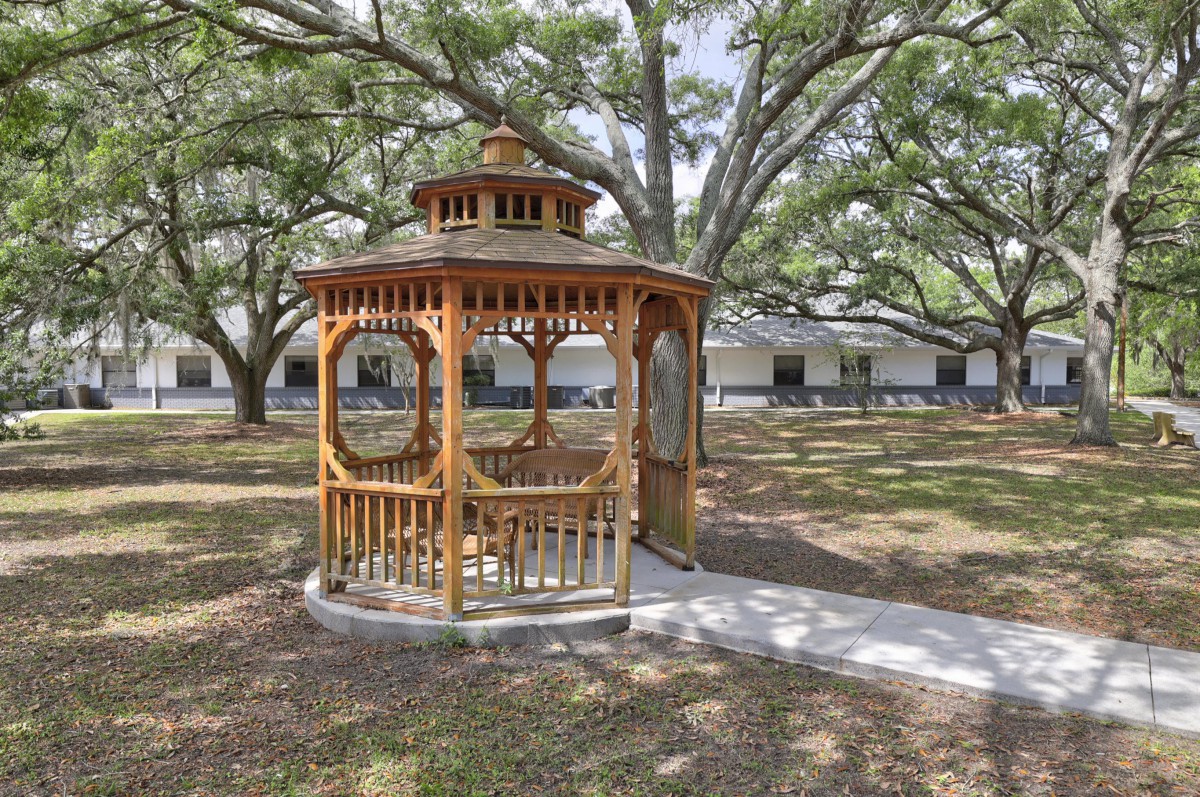 A wooden gazebo situated in a park, surrounded by large trees and a grassy area.