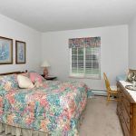 A cozy bedroom with floral bedding, a wooden dresser, and a window letting in natural light.