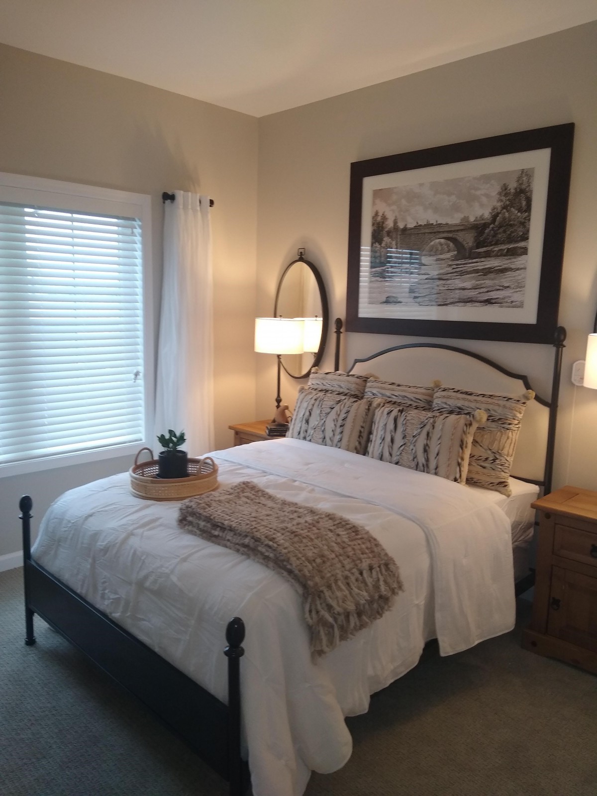 A cozy bedroom with elegant decor, featuring a neatly made bed, flanked by lamps and adorned with framed artwork.