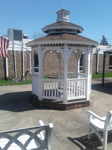 A charming white gazebo in a sunny outdoor setting, complemented by an American flag in the background.