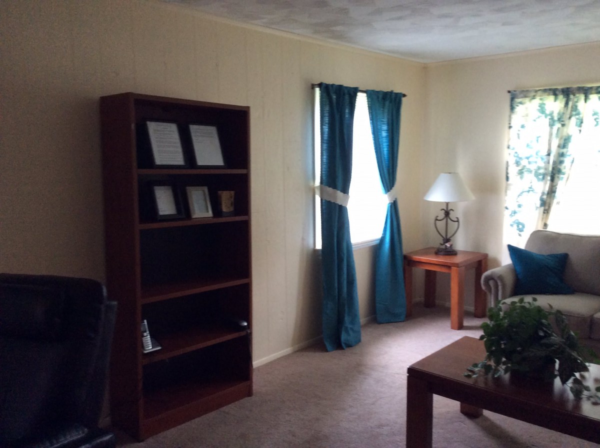 A cozy living room with a bookshelf, blue curtains, and a side table near the window.