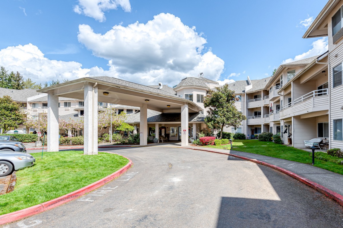 A residential building with a covered entrance and well-maintained landscaping under a partly cloudy sky.