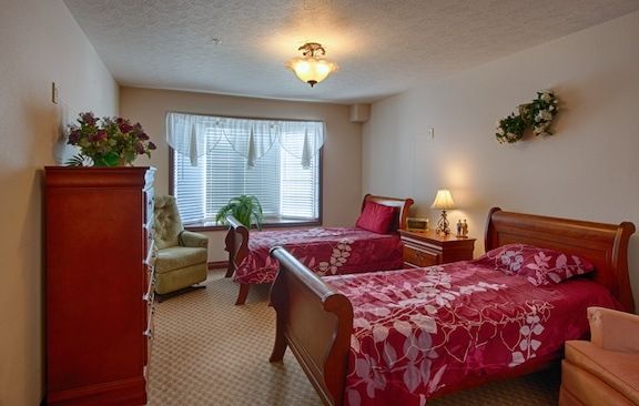 A cozy bedroom with two twin beds adorned with red floral bedding, complemented by warm lighting and decorative plants.