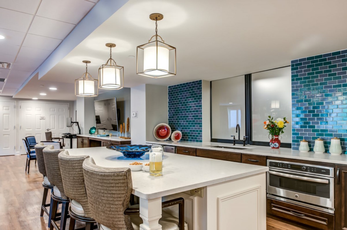 A modern kitchen with a sleek countertop, pendant lights, and stylish bar stools.