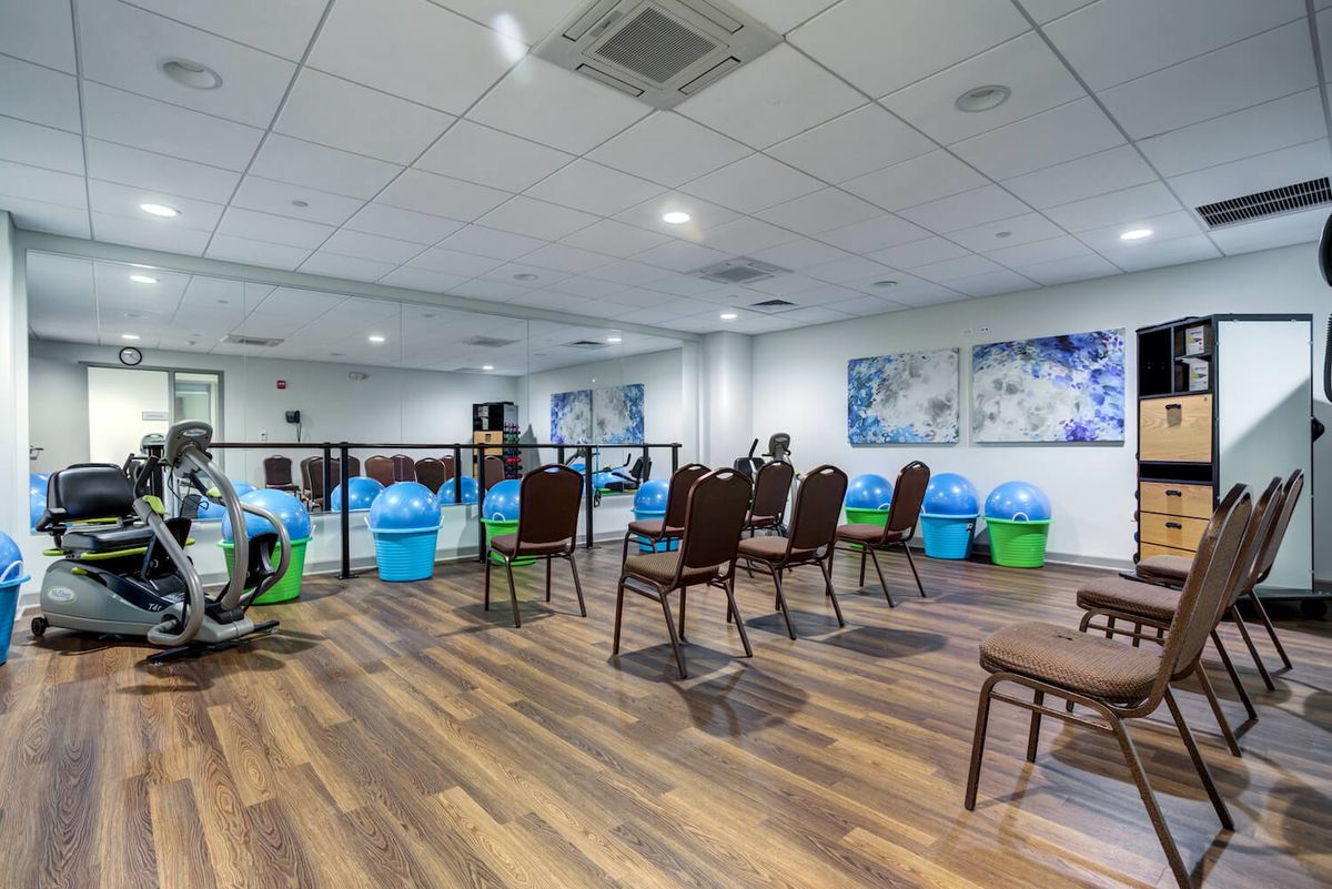 A fitness room equipped with exercise balls, chairs, and mirrors, featuring a wooden floor.