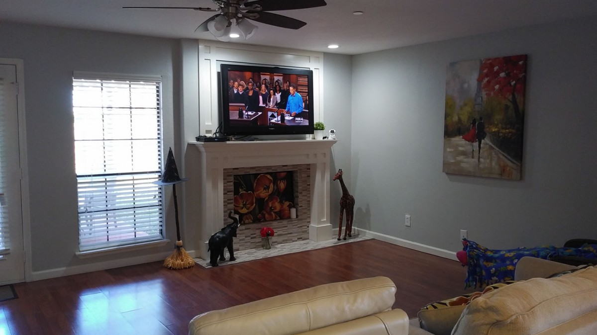 A modern living room featuring a fireplace with a TV mounted above it, giraffe statues on either side, and wooden flooring.