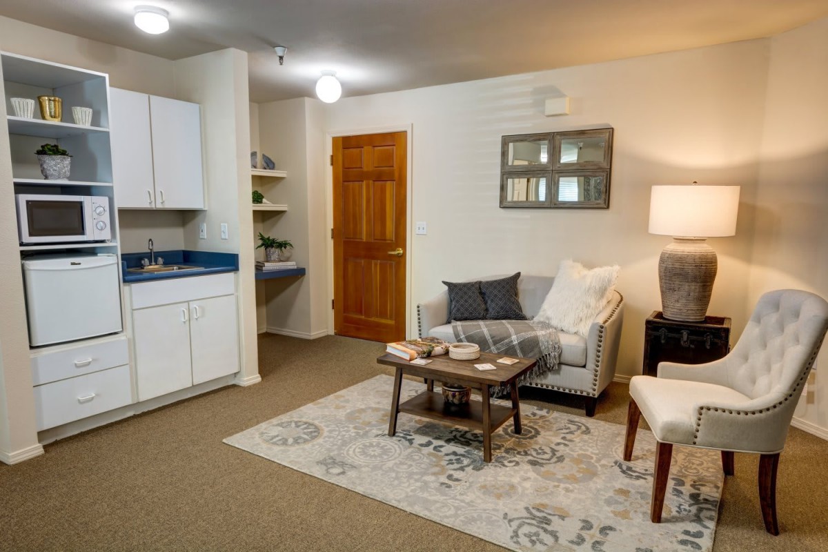 A cozy living room with a sofa, coffee table, and kitchenette area, featuring a warm and inviting ambiance.