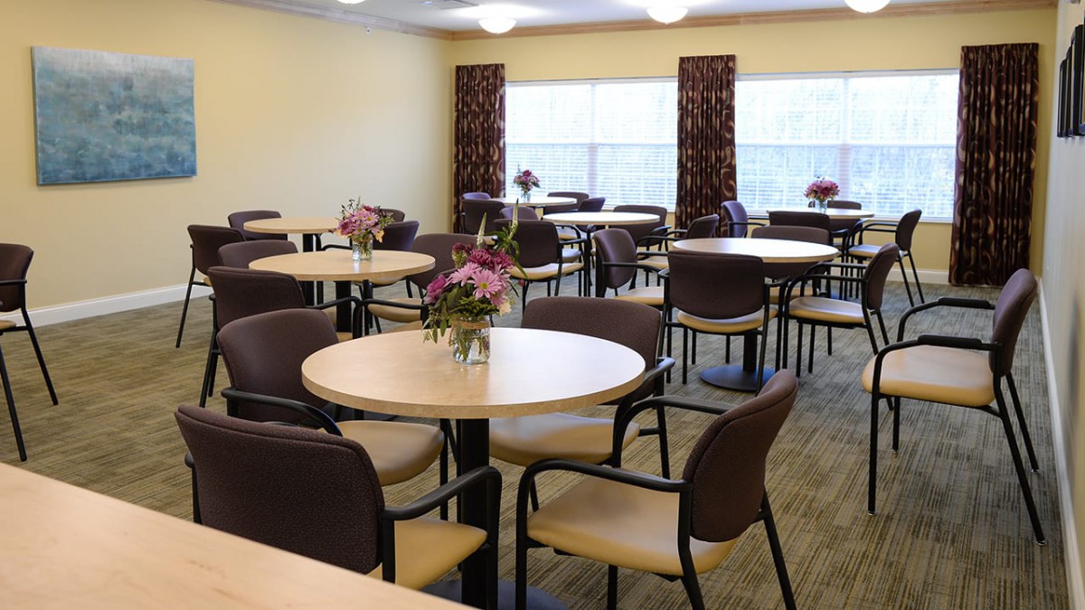 An empty dining room with round tables and chairs, each table adorned with a flower arrangement.