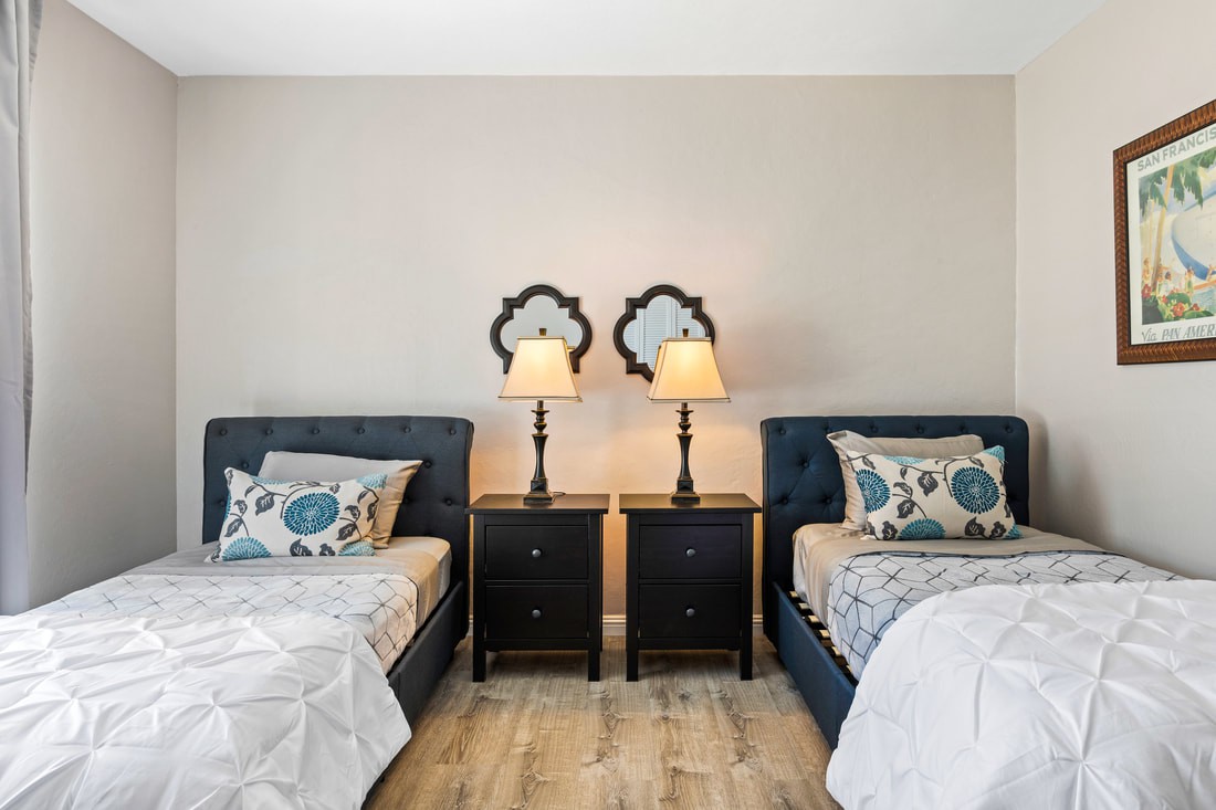 A cozy bedroom with twin beds, each flanked by a nightstand and lamp, featuring stylish decor and patterned pillows.