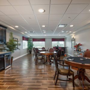 A spacious game room featuring several tables and chairs, with wooden flooring and large windows.