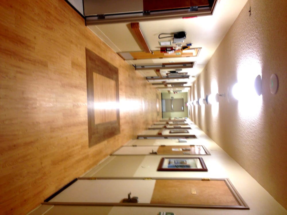 A brightly lit indoor hallway with a wooden floor and several doors on either side.