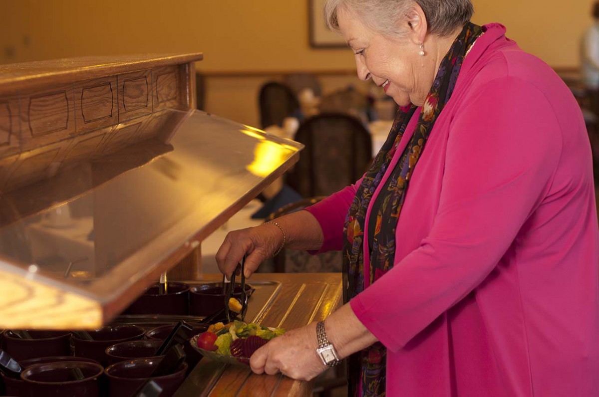 A woman in a pink jacket serves herself at a buffet table indoors.