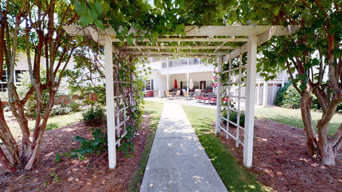 A charming garden pathway leads to an outdoor seating area under a pergola adorned with lush vines.