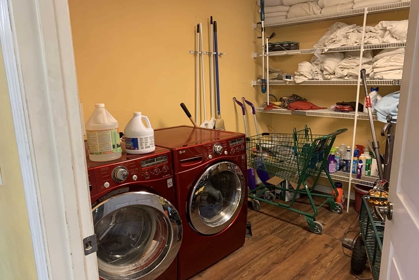 A well-organized laundry room with red washing and drying machines, shelves stocked with cleaning supplies, and various household items.