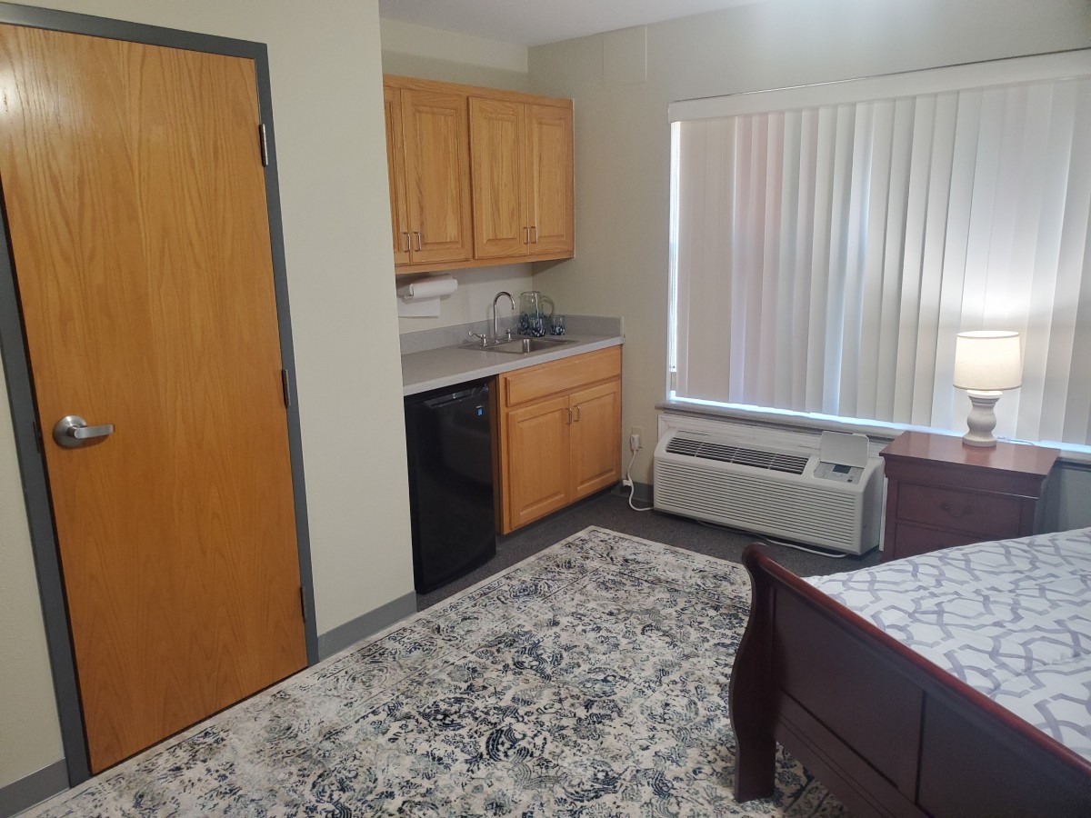 A cozy apartment room featuring a kitchenette with wooden cabinets and a small refrigerator.