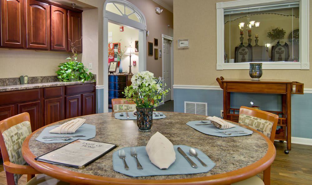 A cozy dining room with a neatly set table featuring folded napkins, cutlery, and a vase of flowers.