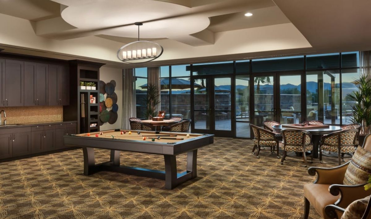 A modern game room featuring a shuffleboard table, stylish furnishings, and large windows allowing natural light.