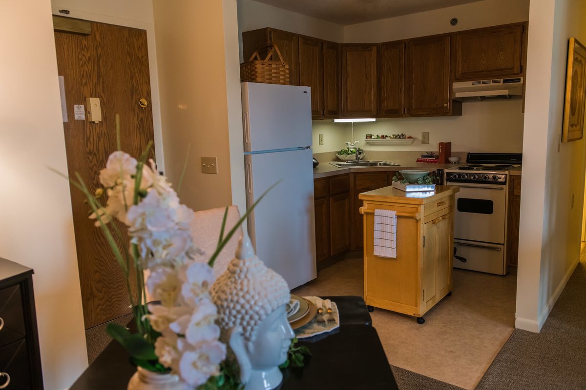 An apartment kitchen with wooden cabinetry, a refrigerator, stove, and decorative elements on the counter.