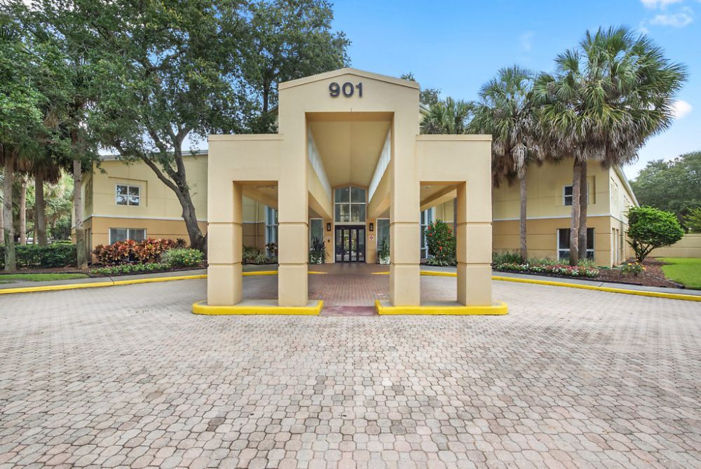 The entrance of a building featuring architectural pillars and surrounded by palm trees.
