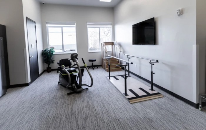 A clean and well-lit therapy room with exercise equipment and a large television on the wall.