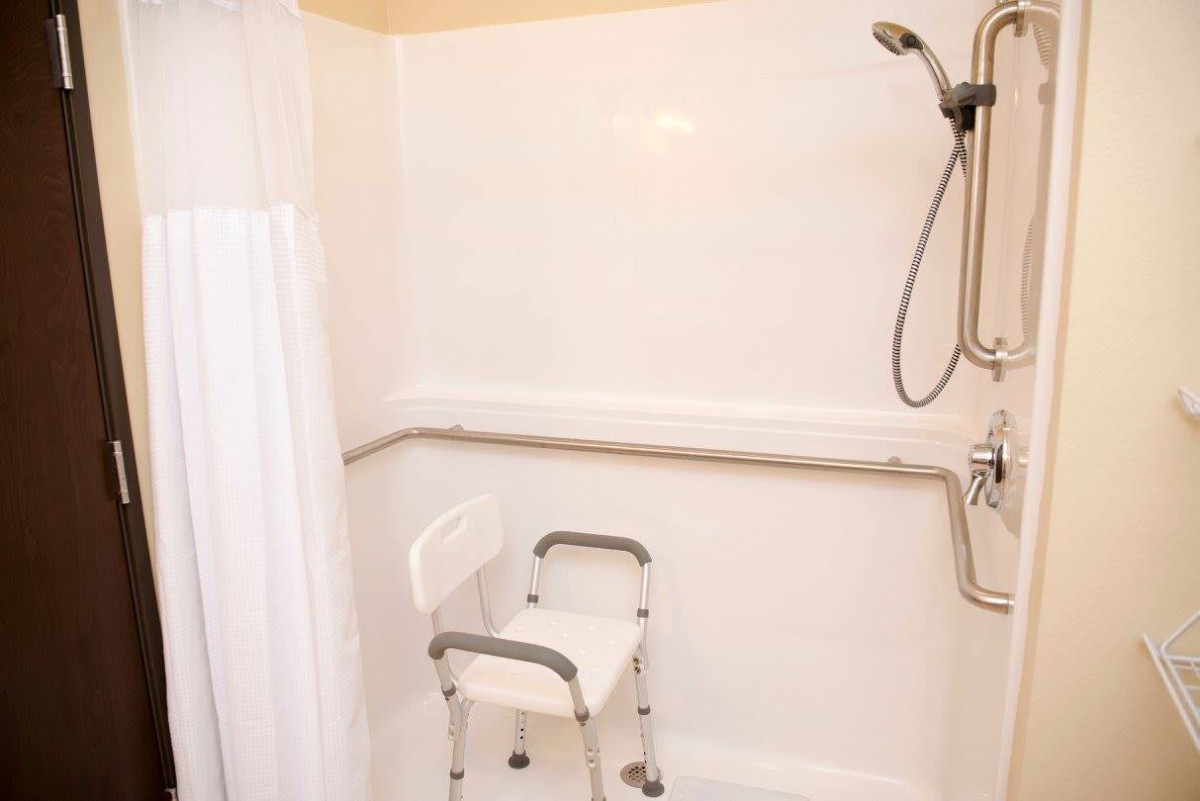 A bathroom featuring an accessible shower with a chair, grab bar, and handheld showerhead.