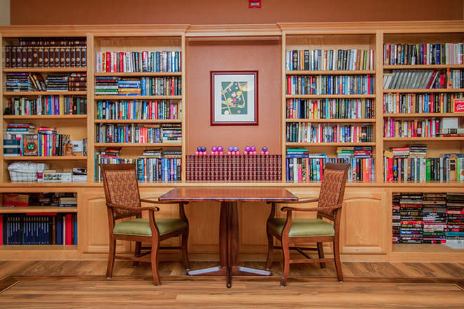 A cozy library corner with wooden bookshelves filled with books, along with a table and two chairs.