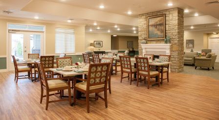 A cozy dining area with neatly arranged tables and chairs, featuring warm lighting and wooden floors.