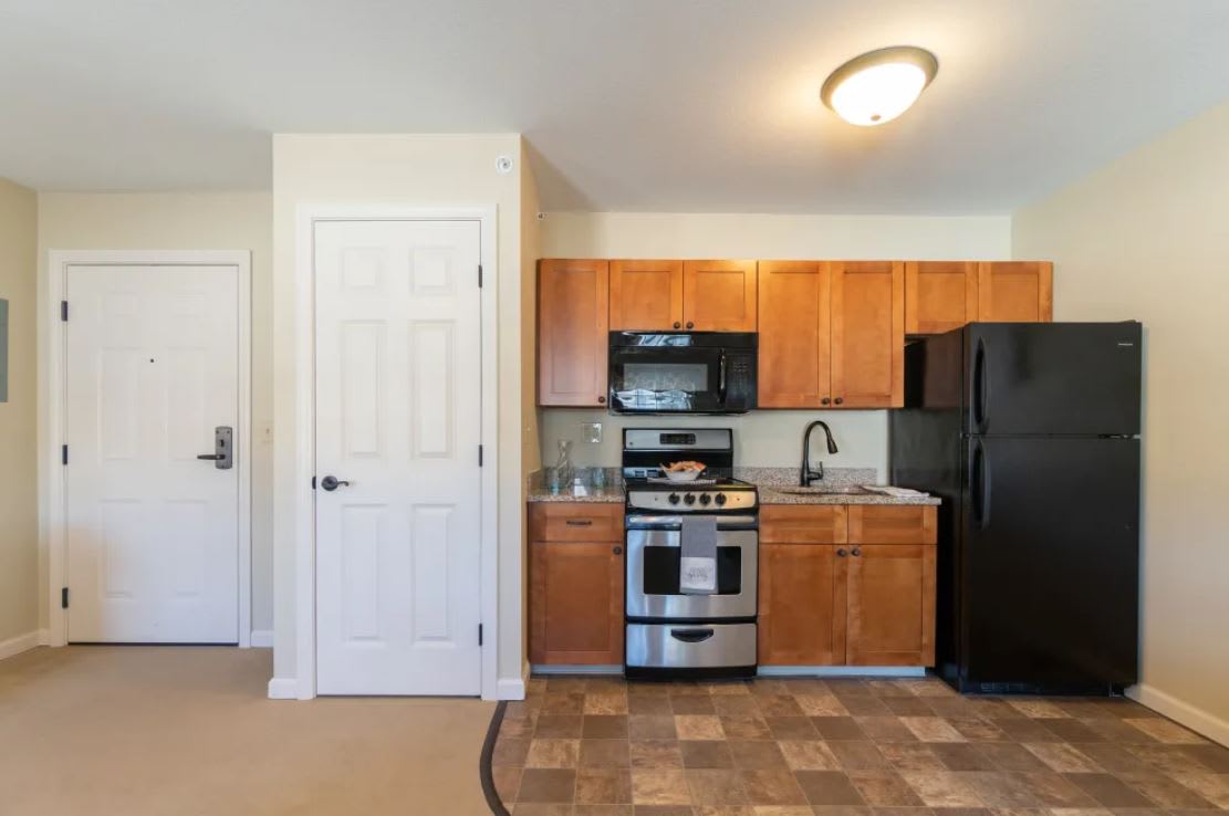 A compact kitchen area in an apartment with wooden cabinets and modern appliances.