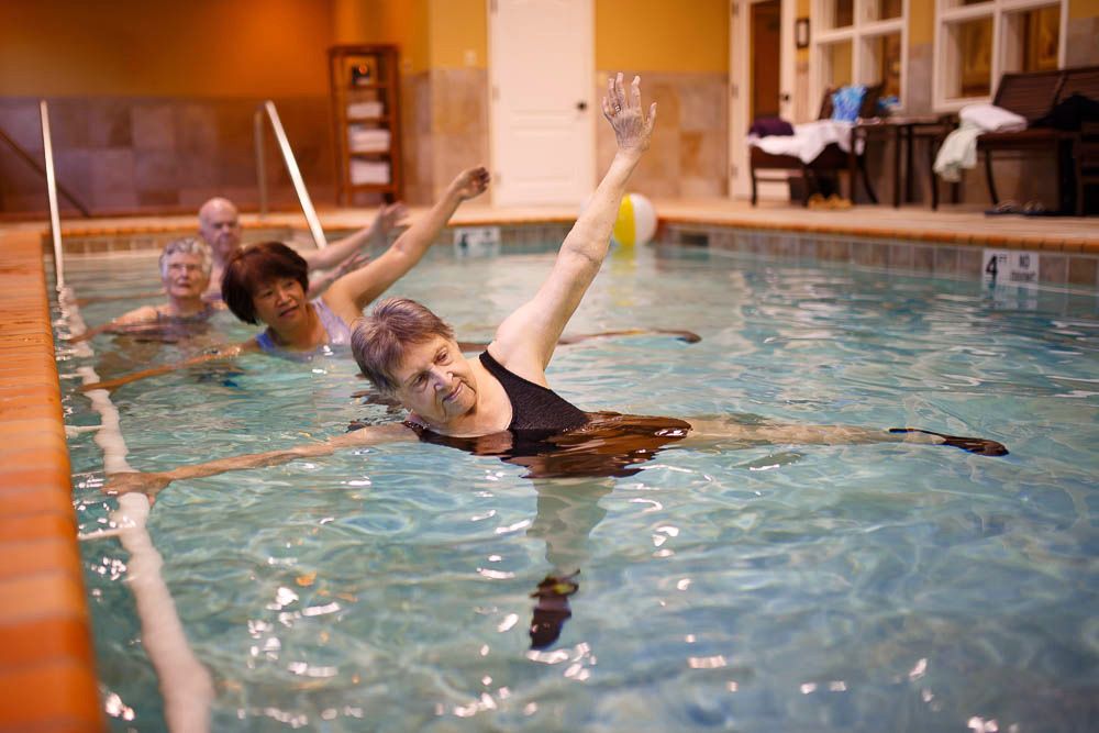 A group of seniors participating in a water aerobics class at an indoor pool.