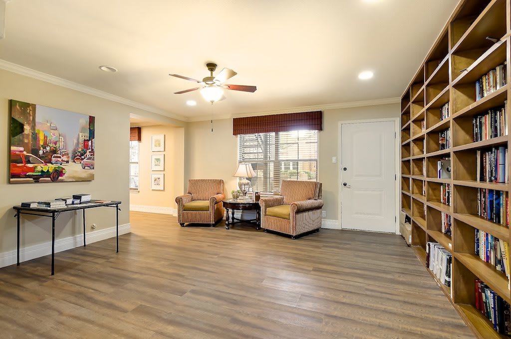 A cozy living room with wood flooring, featuring armchairs, a ceiling fan, and built-in bookshelves.