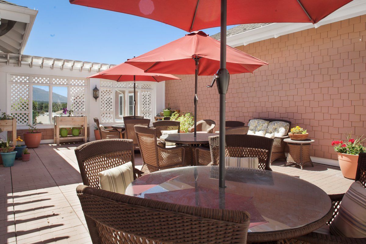 A sunny outdoor patio with wicker furniture and red umbrellas.