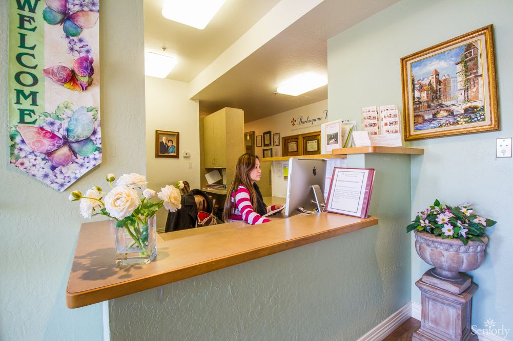 A reception area with a person working at a desk, adorned with flowers and paintings.