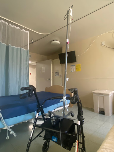 A view of a hospital patient room featuring a bed, walker, and medical equipment.