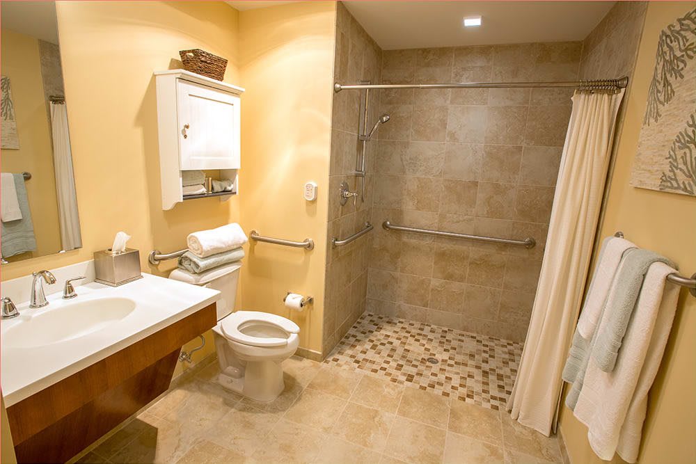 A spacious, accessible bathroom featuring a walk-in shower with handrails and tiled flooring.
