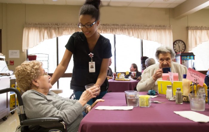 A healthcare professional assists an elderly person in a nursing home setting.