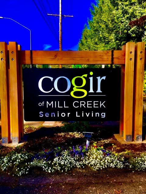 Sign for Cogir at Mill Creek Senior Living, surrounded by greenery.