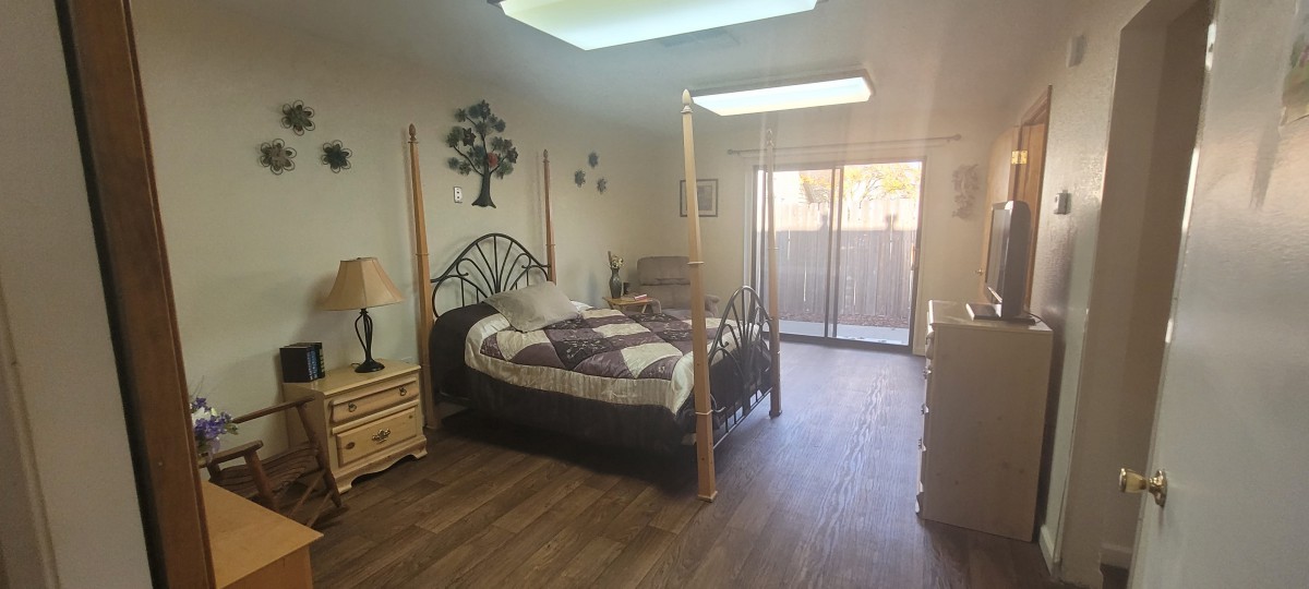 A cozy bedroom with a wooden floor, featuring a four-poster bed, skylight, and sliding glass doors.