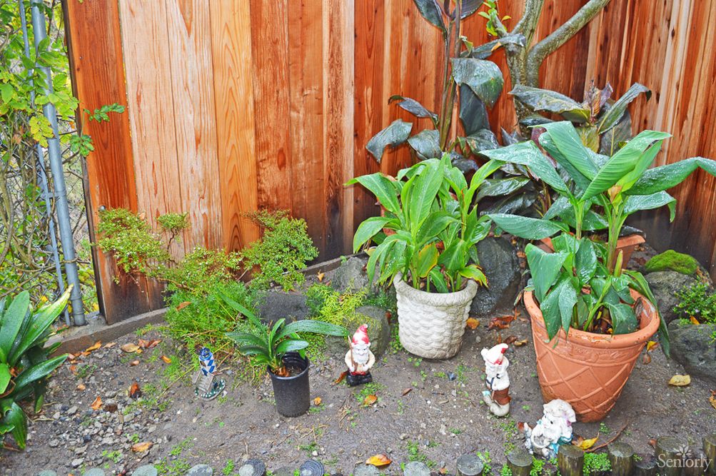 A small garden area with potted plants and decorative figurines against a wooden fence.