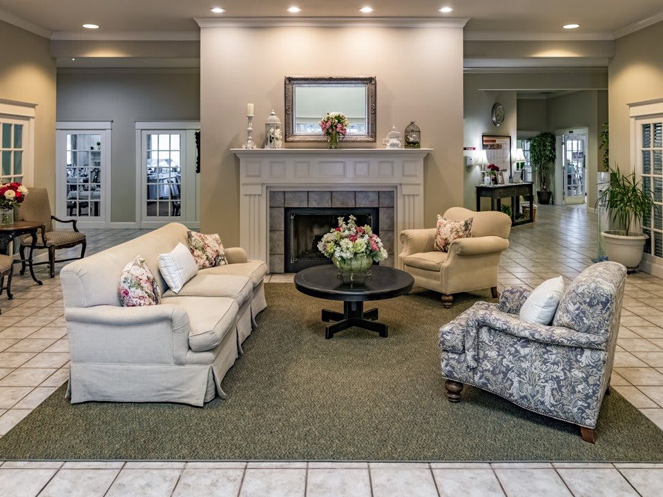 A cozy living room with a fireplace, sofas, armchairs, and a floral centerpiece on the coffee table.