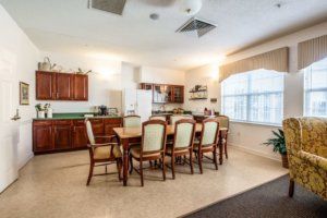 A spacious kitchen and dining area featuring a wooden table with chairs and large windows.