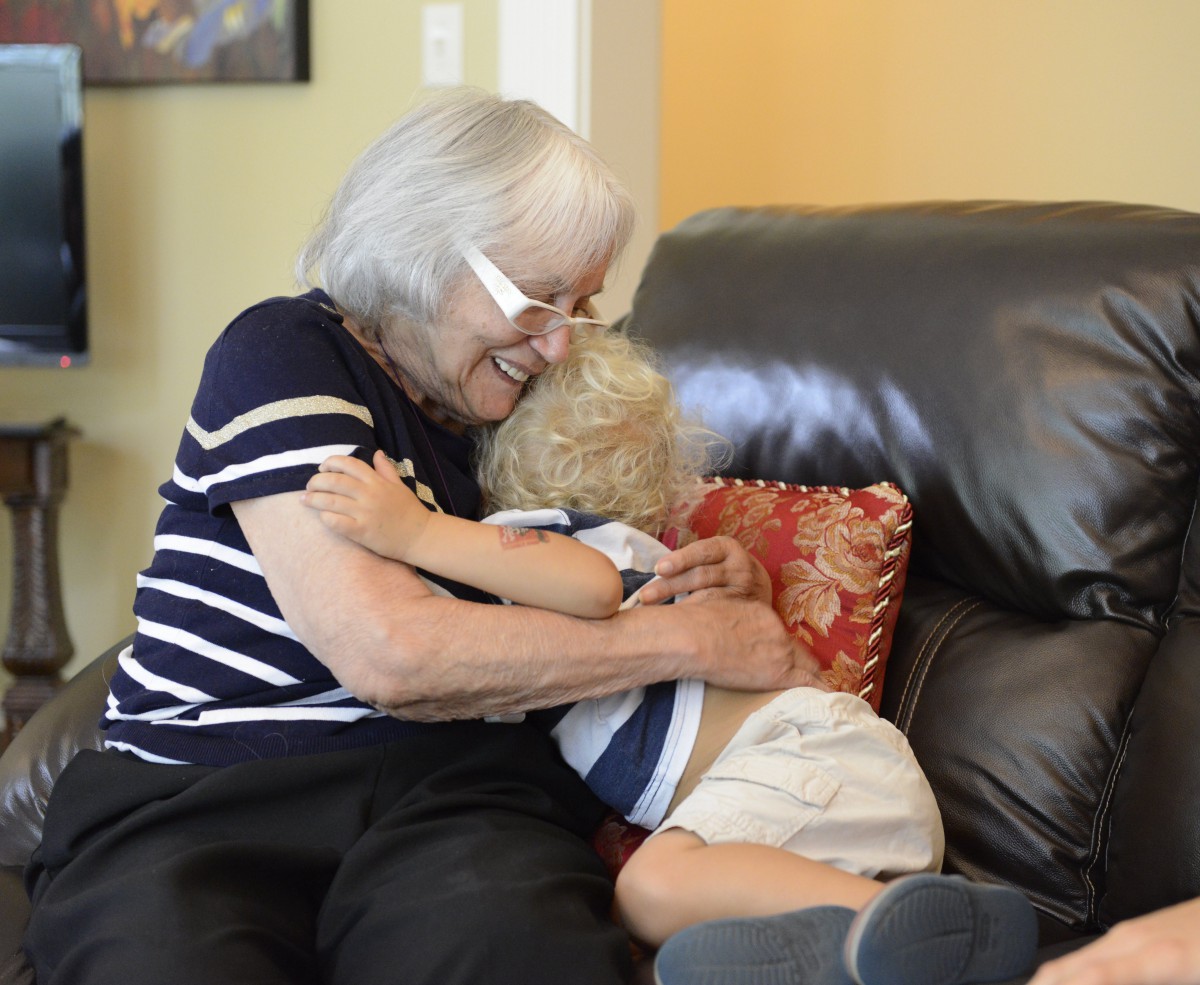 An elderly woman and a young child share a warm hug on the couch.