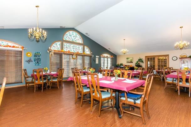 A spacious dining room with neatly arranged tables and chairs, featuring chandeliers and large windows for ample natural light.
