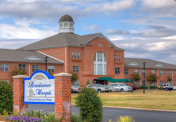 A grand brick hotel with a large entrance and a nearby parking lot under a cloudy sky.