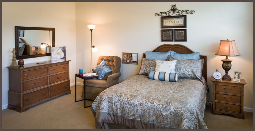 A cozy bedroom with a neatly made bed, an upholstered chair, and a standing lamp.