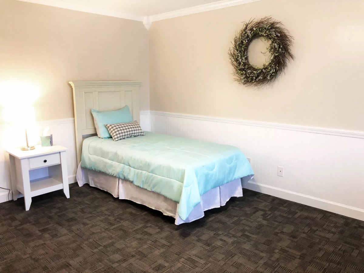 A minimalist bedroom with a pastel-colored single bed and a wreath hanging on the wall.