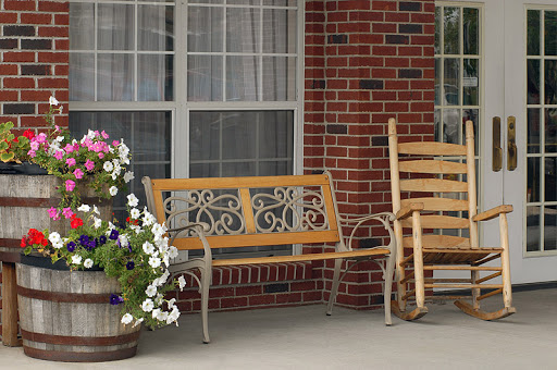 A cozy outdoor setting featuring wooden benches, a flower pot filled with vibrant flowers, and a brick wall backdrop.
